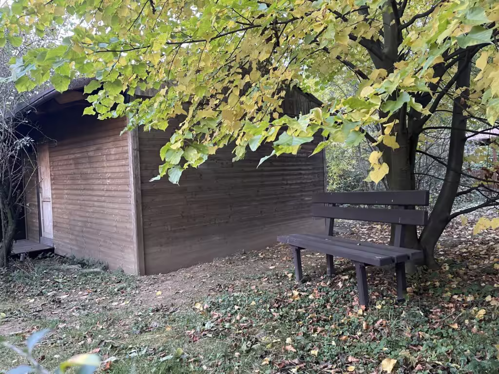 Lavička pod lípou u dřevěné chatky pro pobyt ve tmě